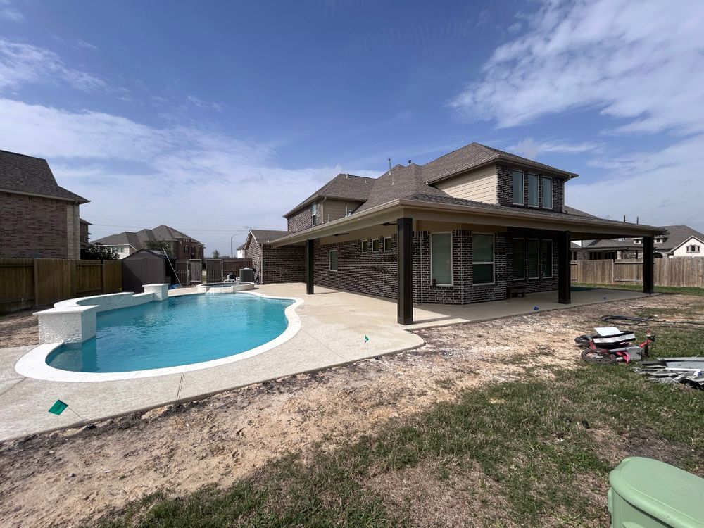 Backyard with a pool, covered patio, brick house, and a blue sky.
