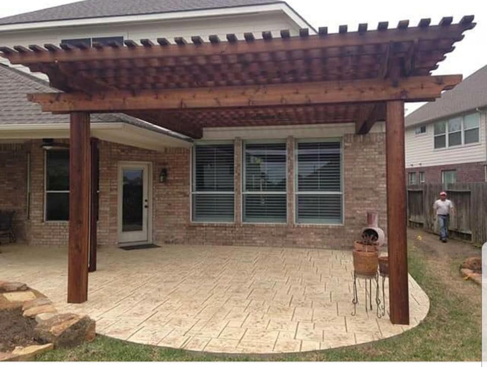 Wooden pergola over a stamped concrete patio, adjacent to a brick house.