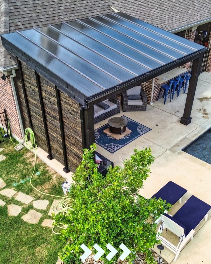 Pergola with dark roof over patio furniture, next to a pool.