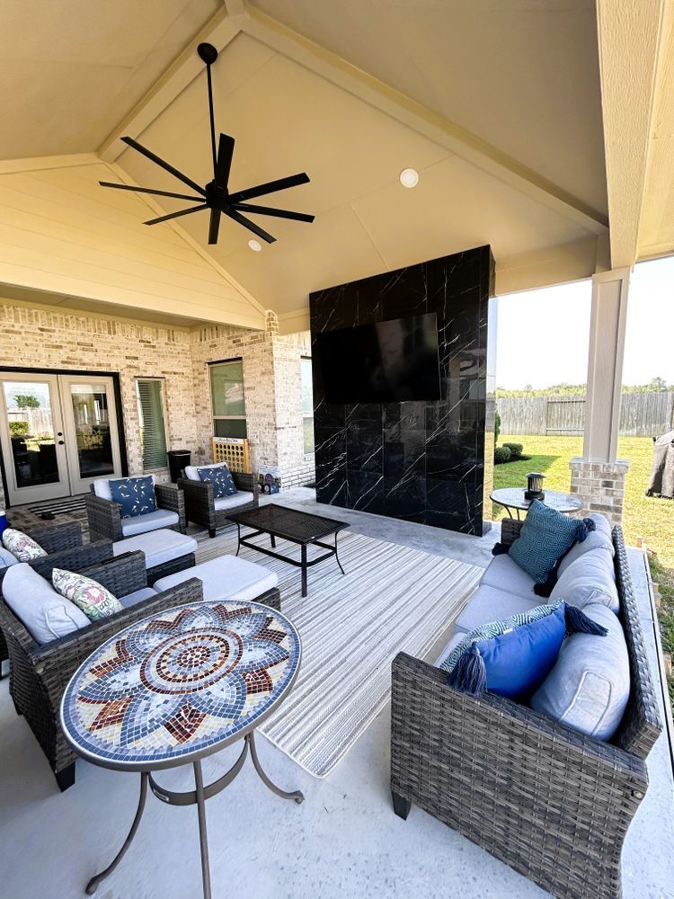 Outdoor living space with seating, TV on a black marble wall, and a ceiling fan.