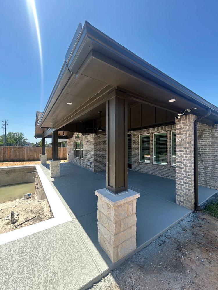 Covered patio of a brick house with brown columns, overlooking a pool under construction.