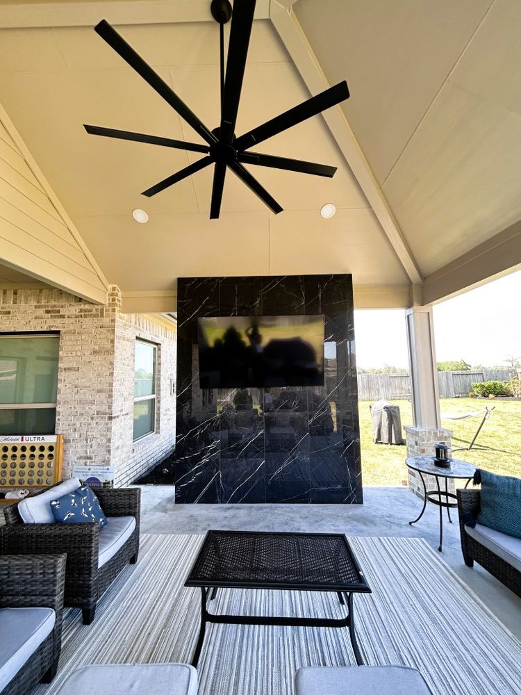 Outdoor patio with black and white tiled TV wall, seating, and large fan.