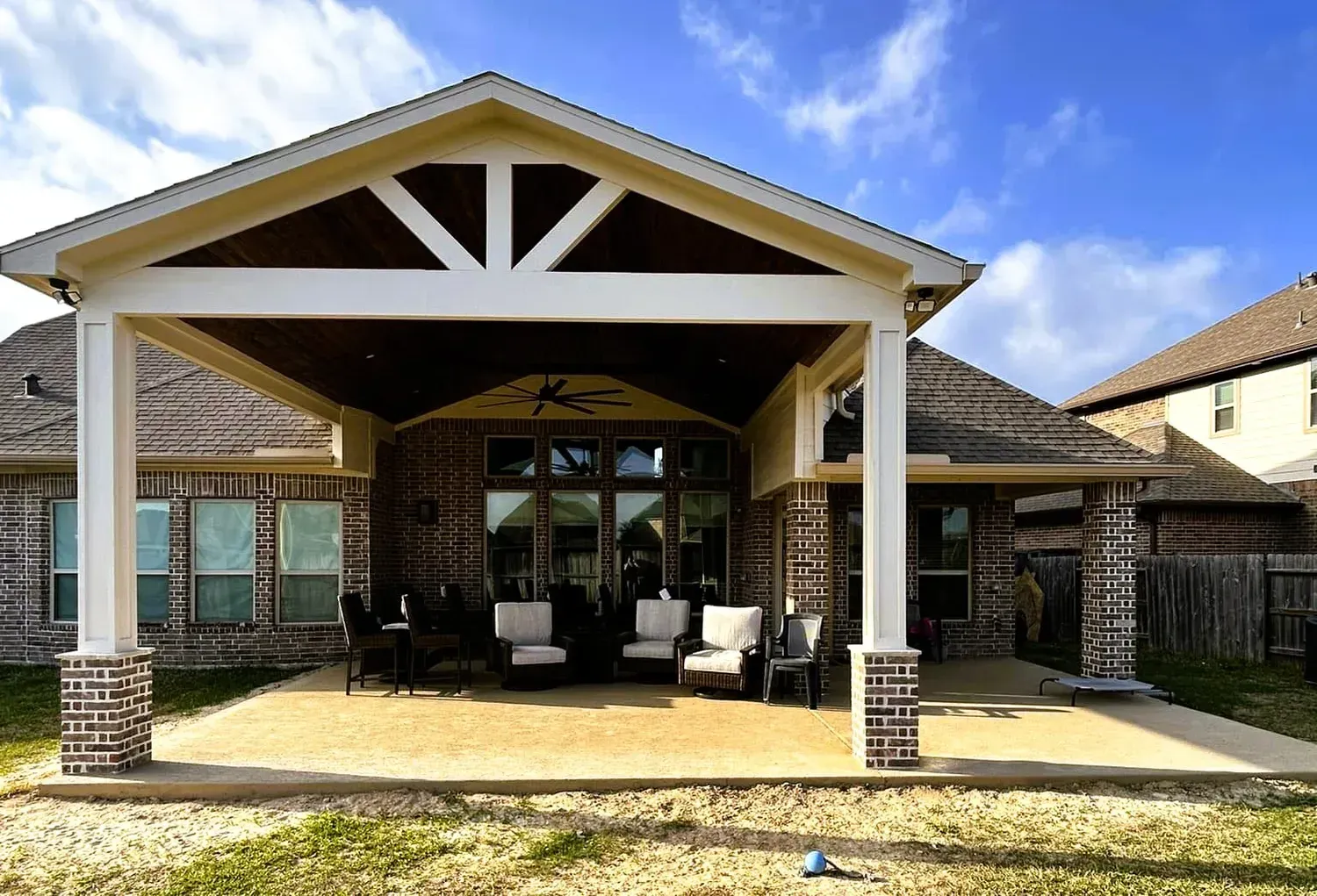 Covered patio with brick columns, seating, and a brick house.