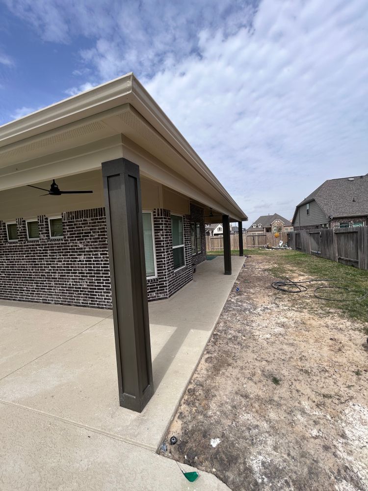 A covered patio with dark columns, brick wall, and concrete floor under a cloudy sky.