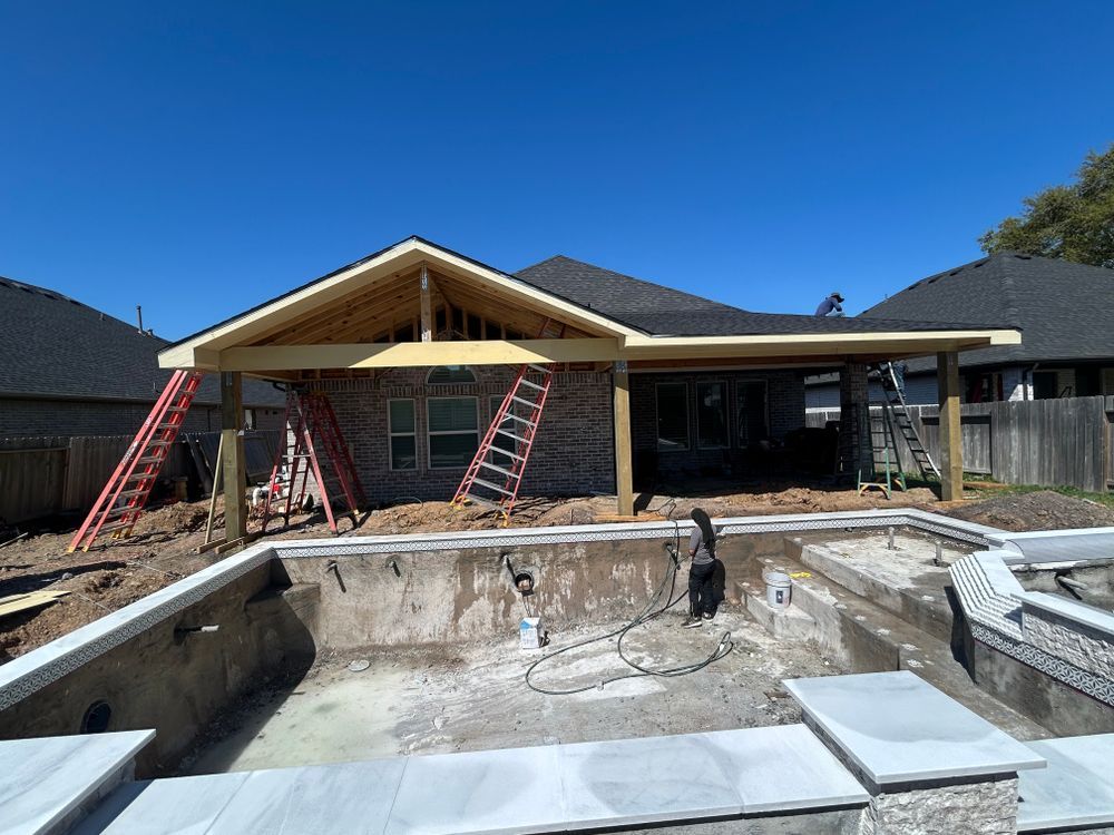 Construction of a patio cover next to an unfinished swimming pool. Bright blue sky.