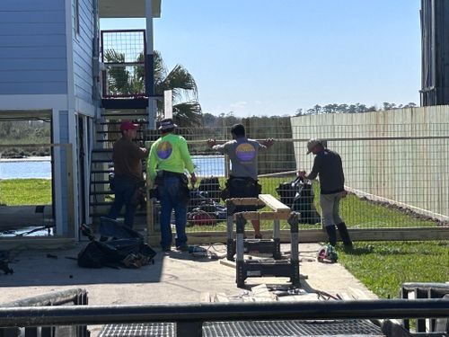Construction workers building a fence near a light blue building. One uses a saw.