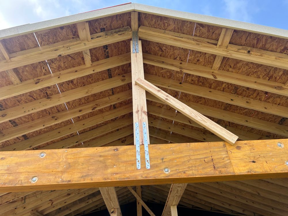 Wooden roof frame construction with support beams and trusses against a blue sky.