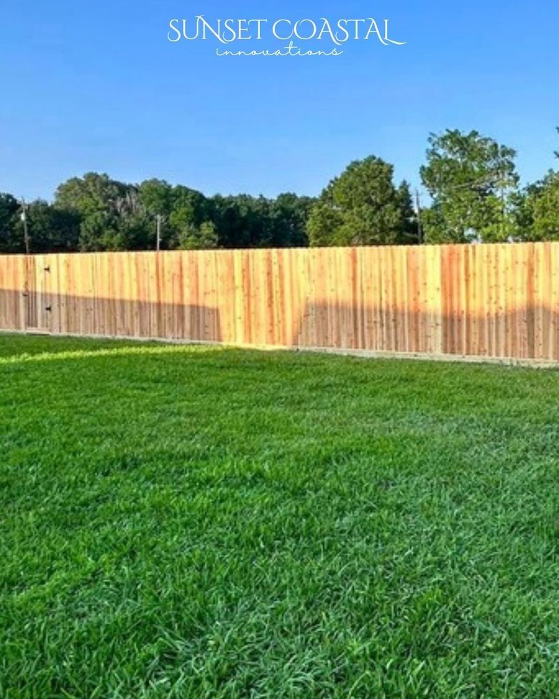 Green grassy lawn with a wooden fence, trees, and blue sky.