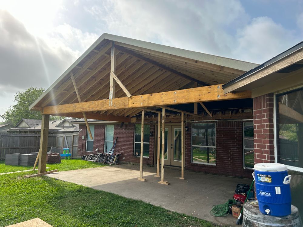 Construction of a wooden patio cover attached to a brick house; blue sky.