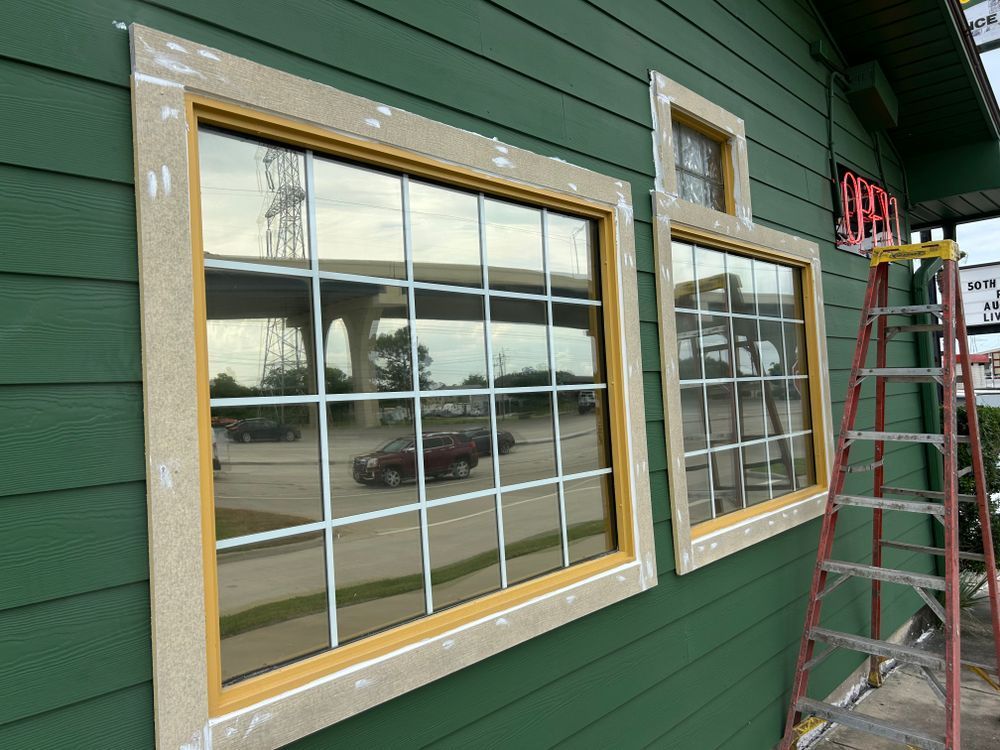 Green building exterior with windows, reflecting a street scene, and a ladder.