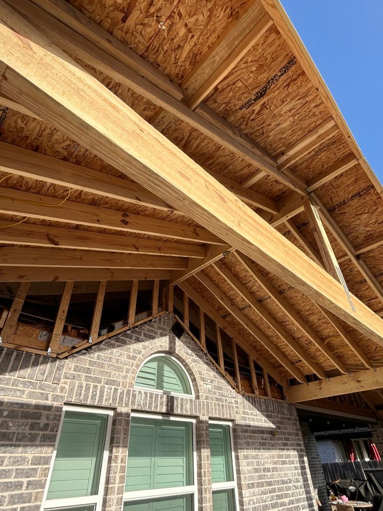 Wooden rafters and OSB roof decking over a brick house, view from below on a sunny day.