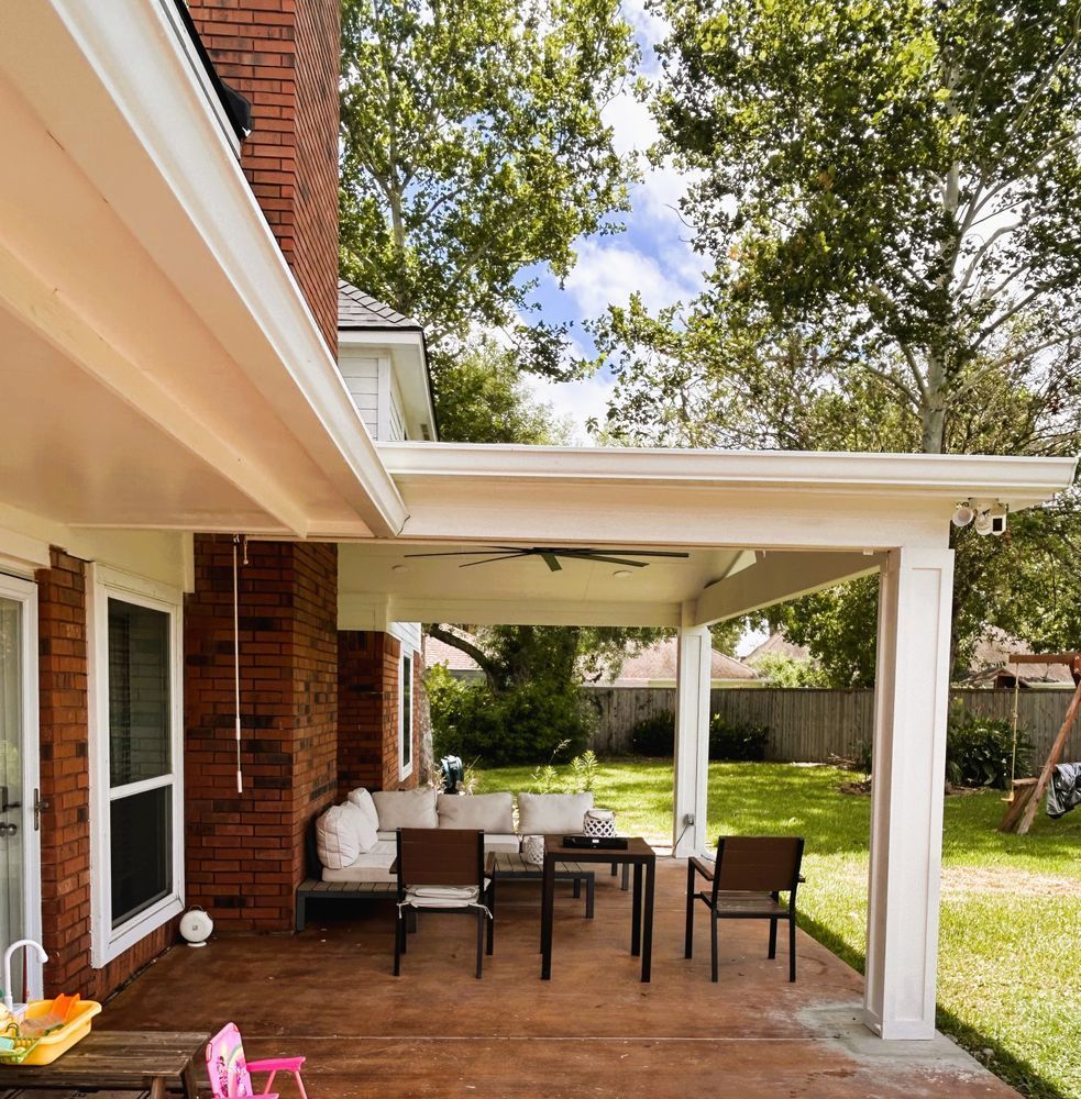 Covered patio with furniture, brick house, and green lawn.