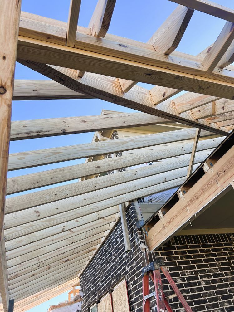 Wooden roof framing against a blue sky, partially covering a brick building.