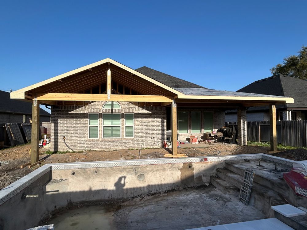 Backyard with unfinished pool and a new wooden patio cover attached to a brick home.