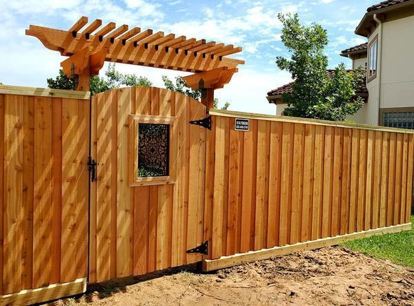Wooden fence with arbor gate, natural wood color, in front of a house with green grass.
