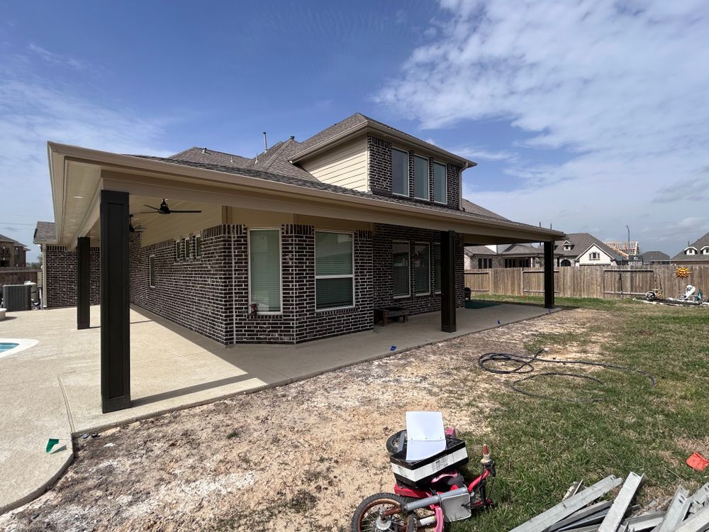 House exterior with a covered patio, brick walls, and a grassy backyard on a sunny day.