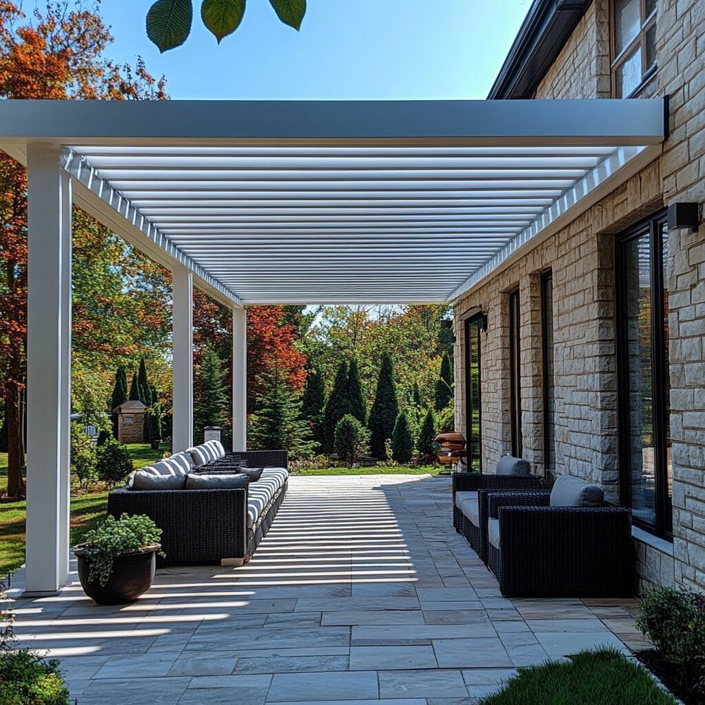 Outdoor patio with white pergola, seating, and stone pavers; trees in the background.