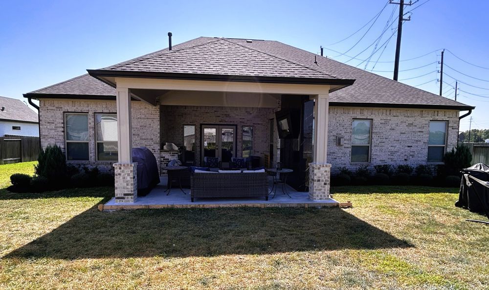 Backyard patio with outdoor furniture under a covered area, house in background.
