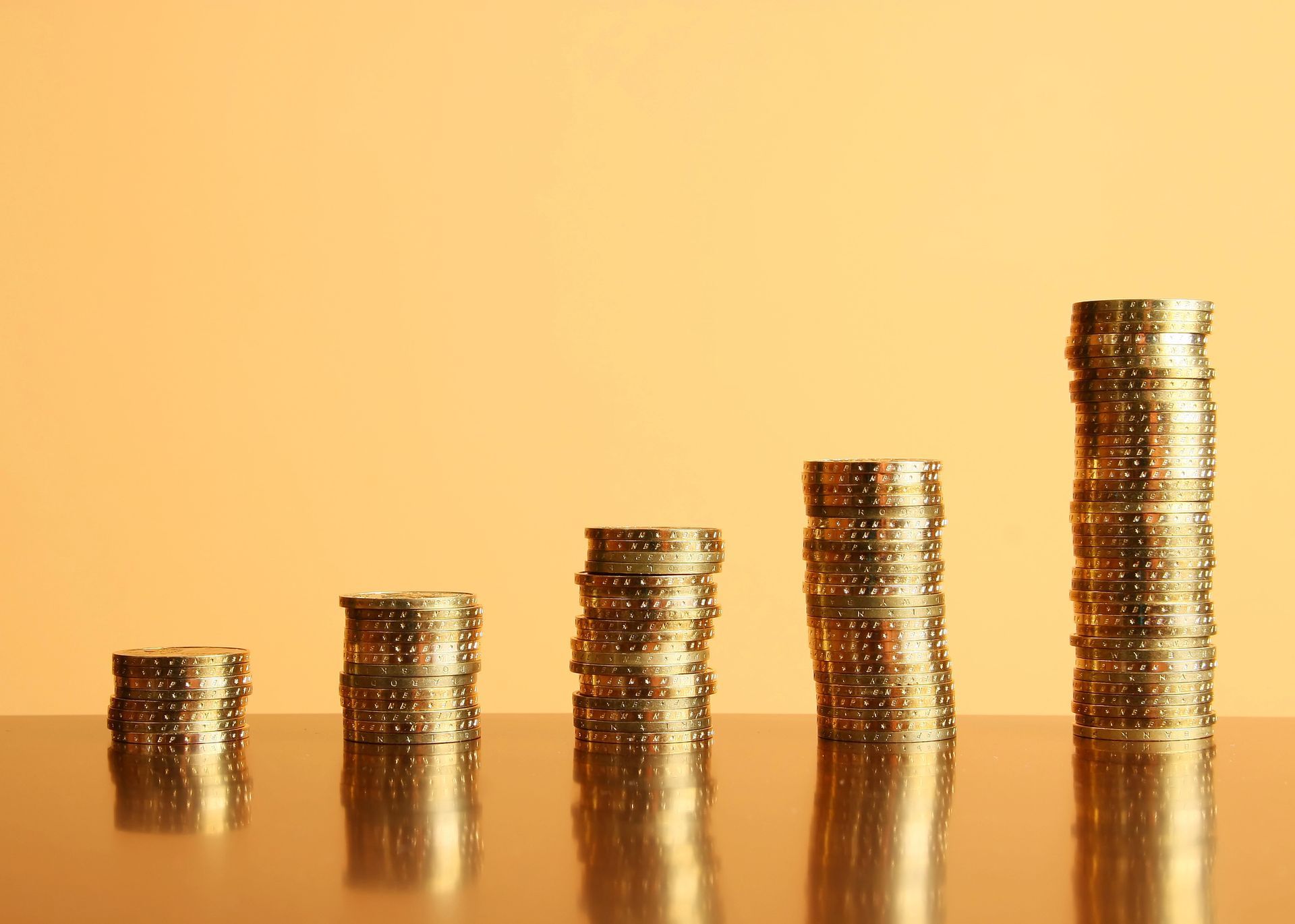 Pile di monete d'oro disposte in ordine crescente, a suggerire la crescita finanziaria, su uno sfondo dorato.