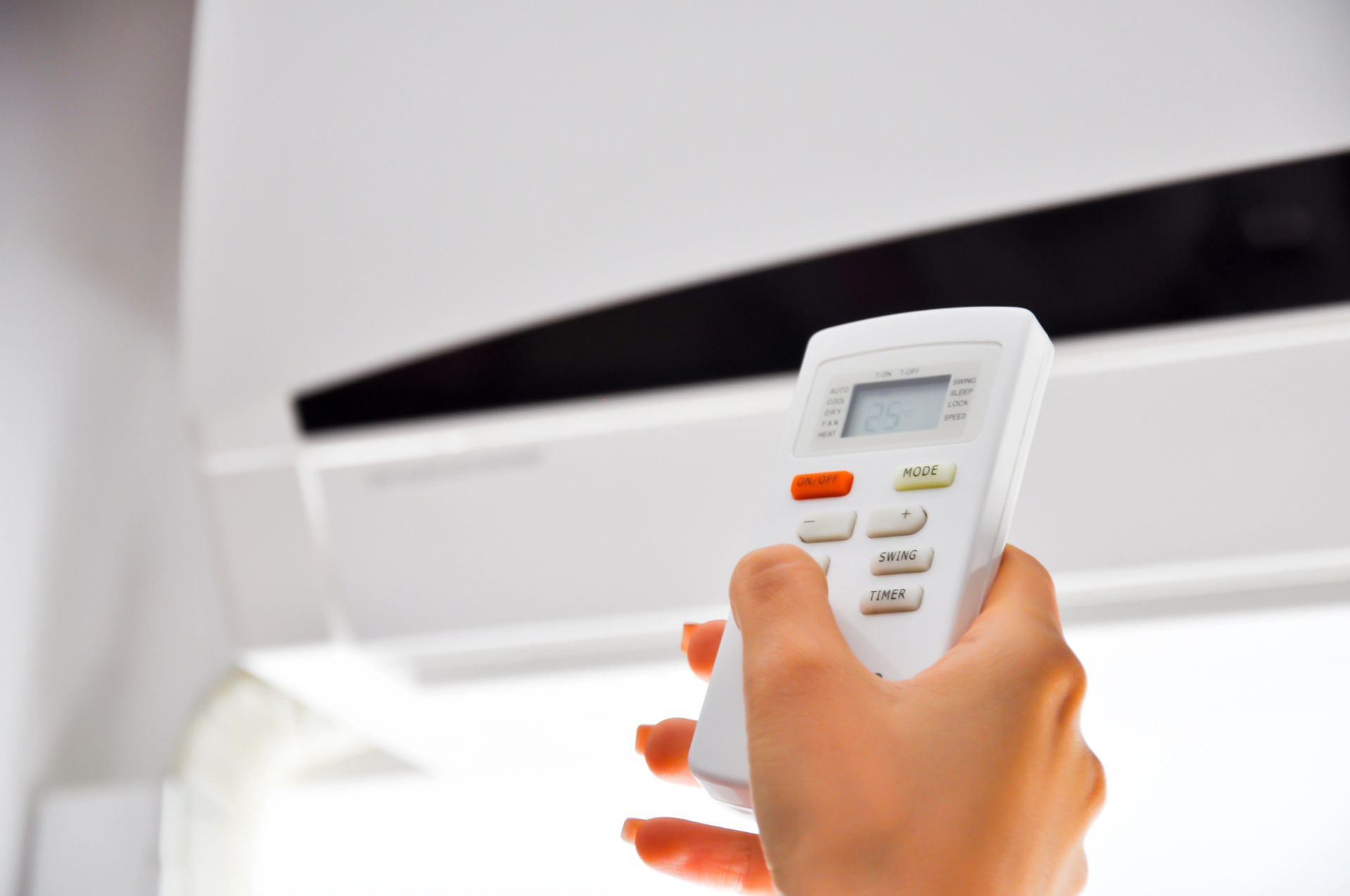 Mano che tiene un telecomando bianco e lo punta verso un condizionatore bianco.