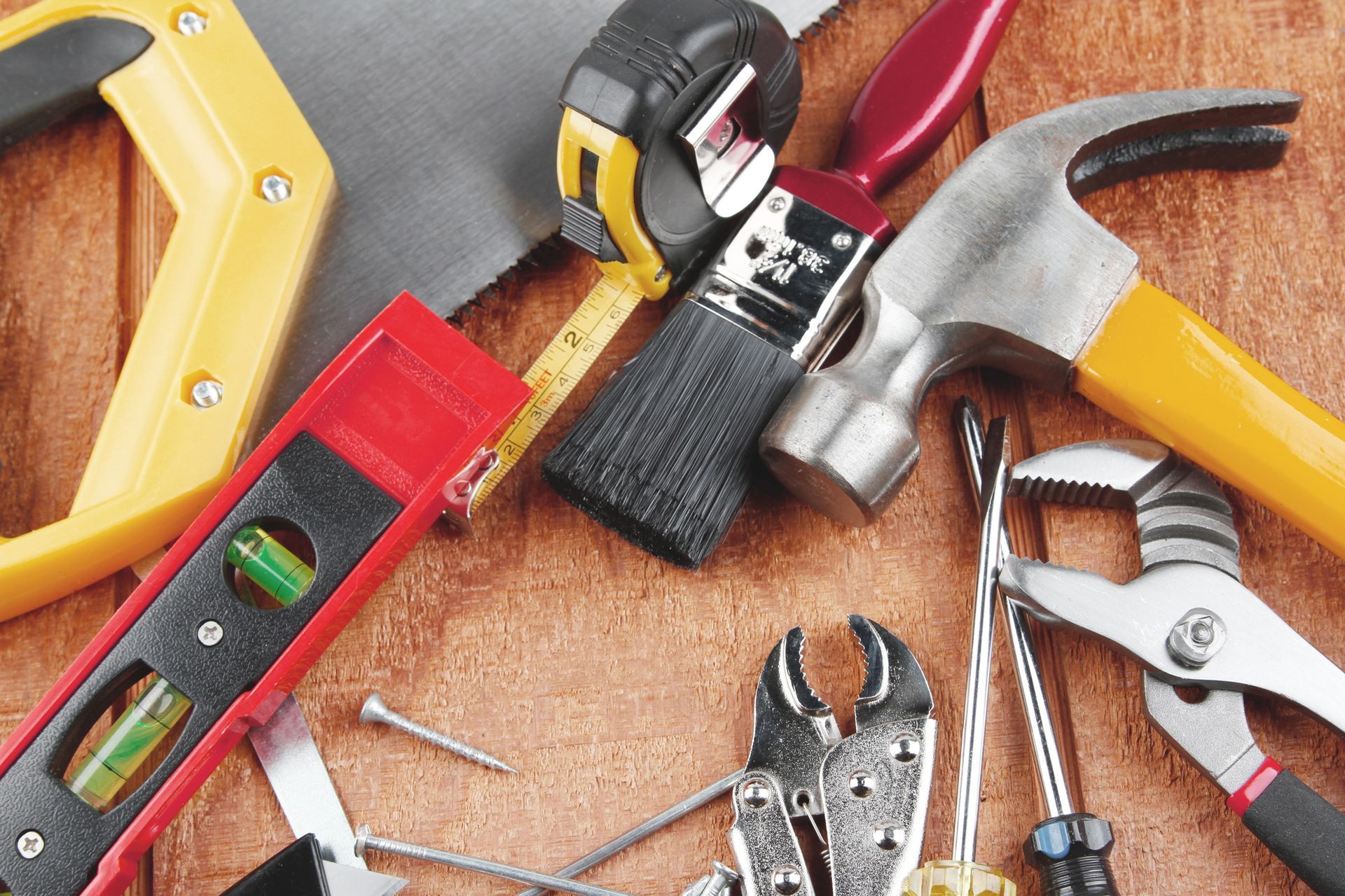 Vari utensili manuali: martello, livella, metro a nastro, pinze, cacciavite e pennello su legno.