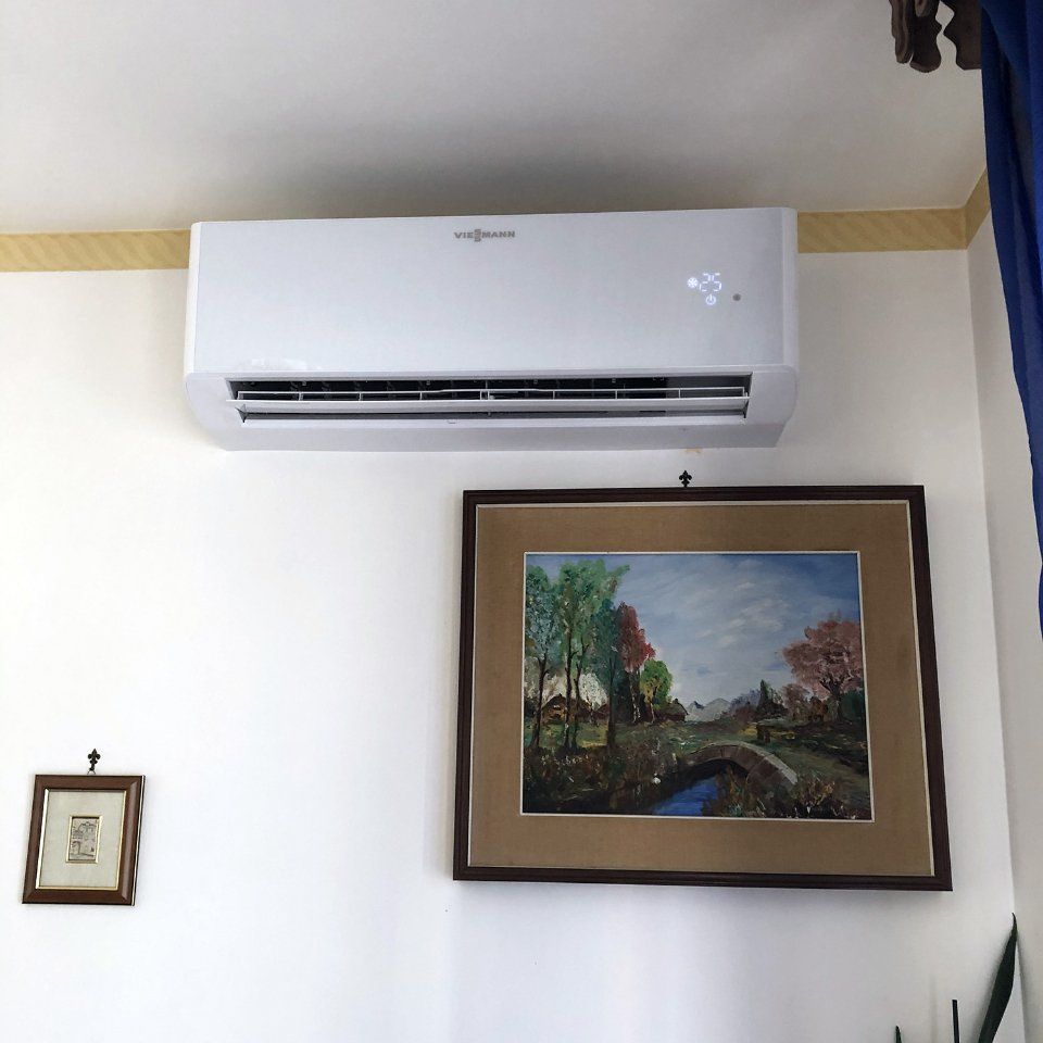 Unità di aria condizionata bianca sopra un dipinto paesaggistico incorniciato su una parete bianca.