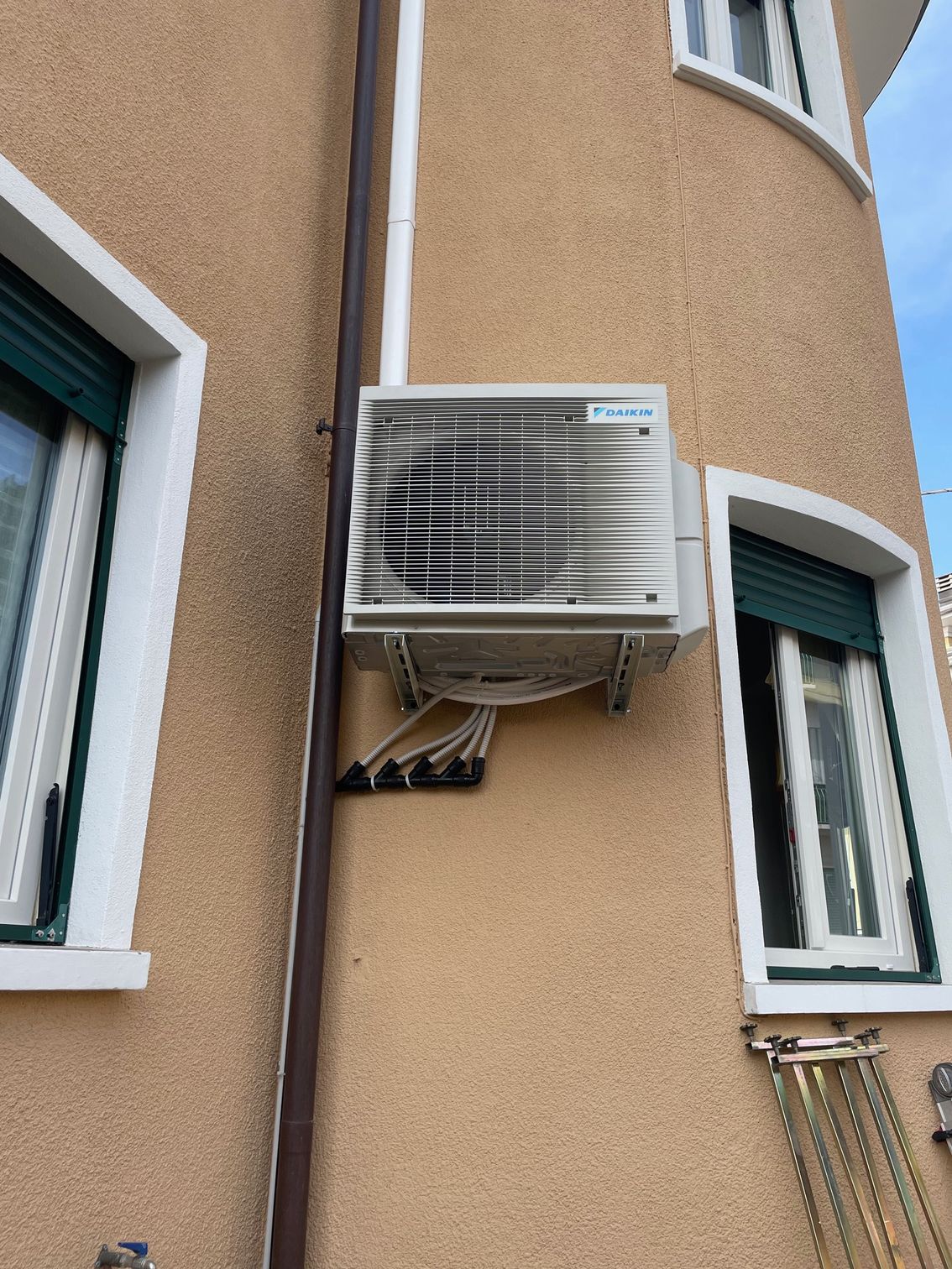 Un condizionatore d'aria Daikin esterno montato su un edificio marrone chiaro accanto a due finestre.