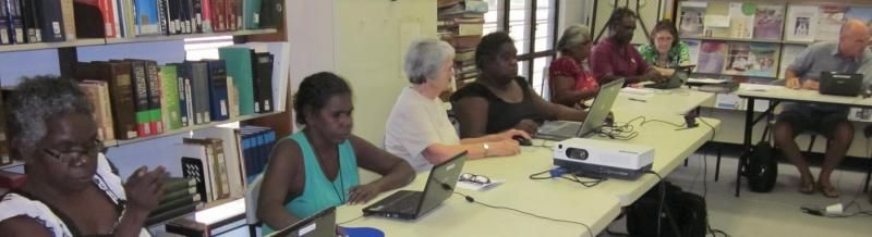 A group of people are sitting around a table with laptops.