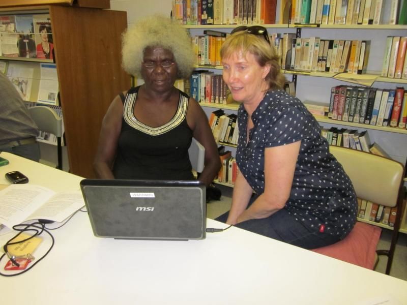 Two women sit at a table in front of a dell laptop