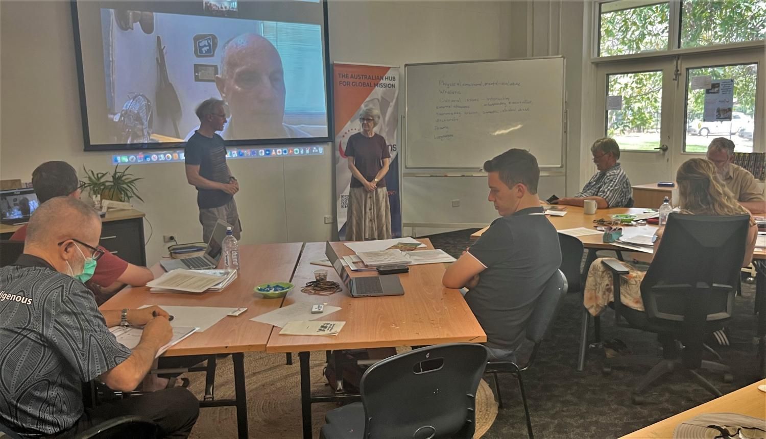 A group of people are sitting at tables in a room watching a presentation.