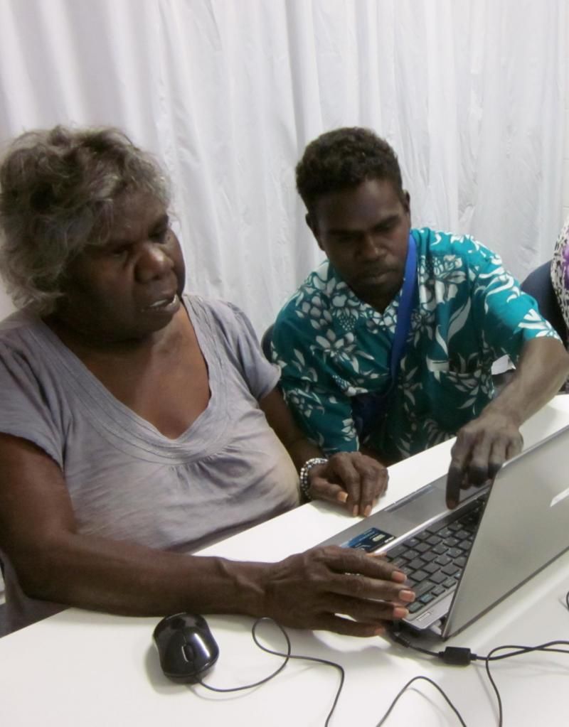 A man and a woman are sitting at a table looking at a laptop