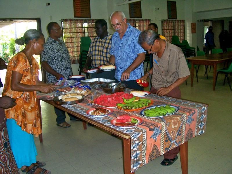 A group of people standing around a table with plates of food on it