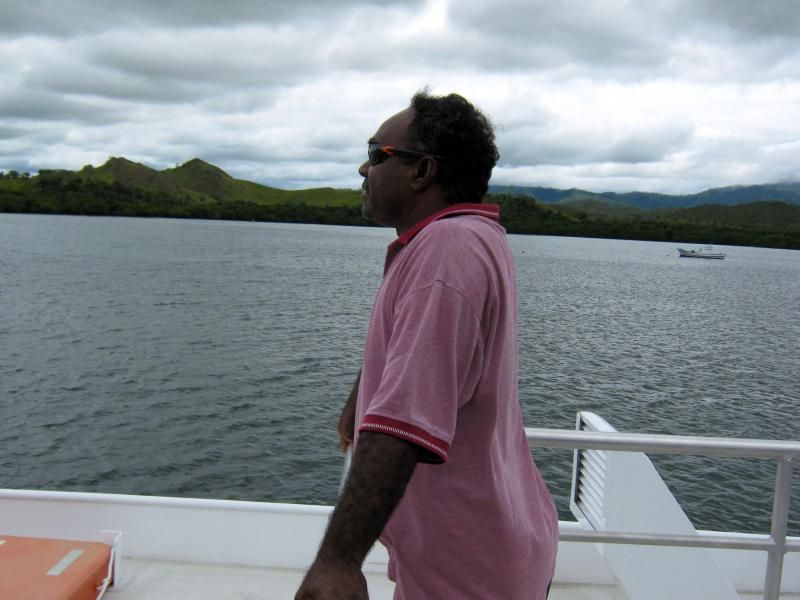 A man in a pink shirt stands on a boat looking at the water
