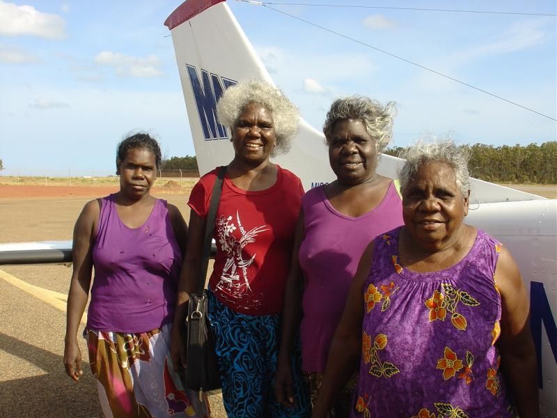 A group of women standing in front of a plane with the letter m on the tail