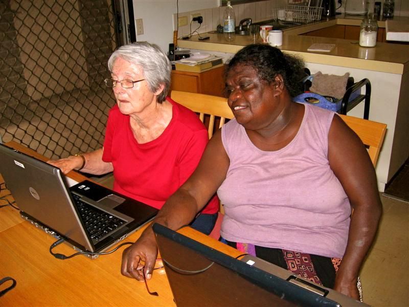Two women are sitting at a table using laptops