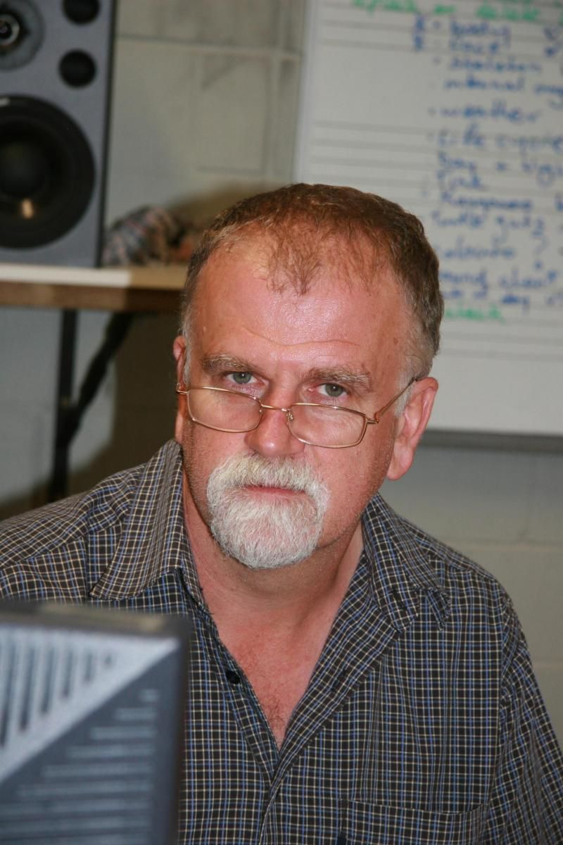 A man with glasses and a beard is sitting in front of a computer monitor.
