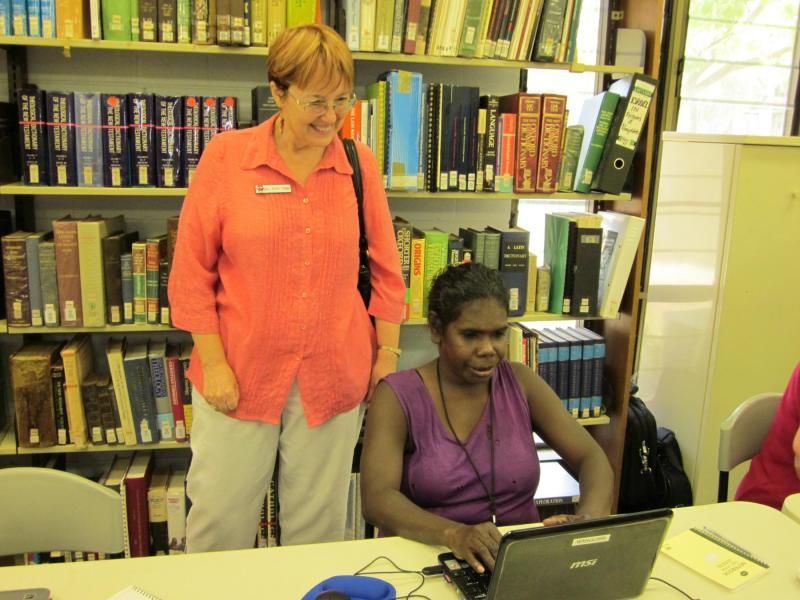 A woman standing next to a woman using a laptop