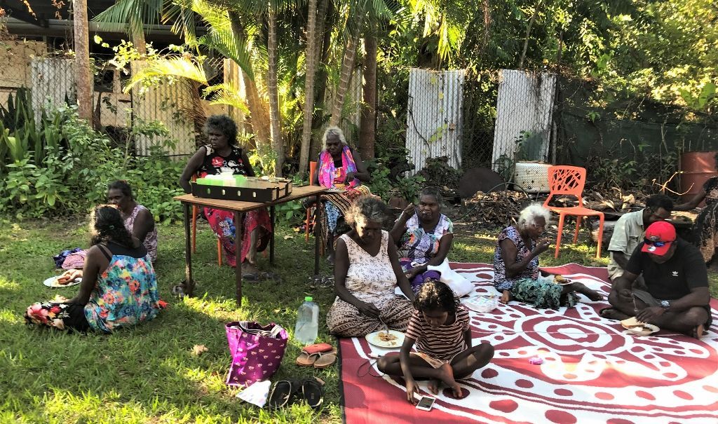 A group of people are sitting on a rug in the grass.