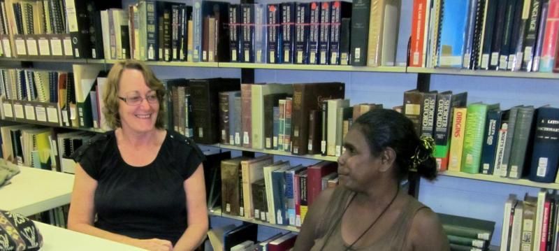 Two women are sitting in front of a bookshelf in a library