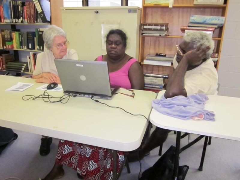 Three women sit at a table looking at a laptop