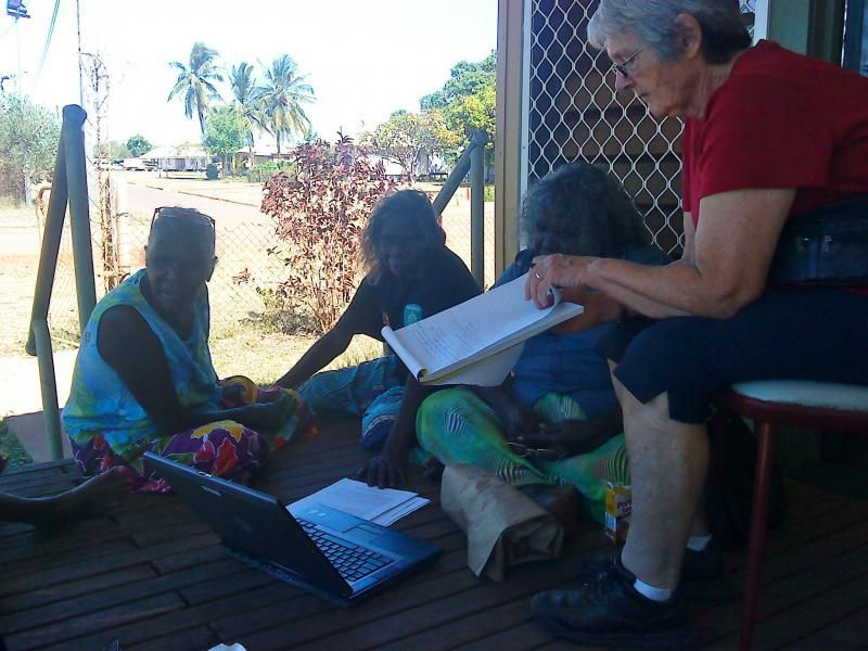 A woman in a red shirt is sitting on a porch looking at a laptop