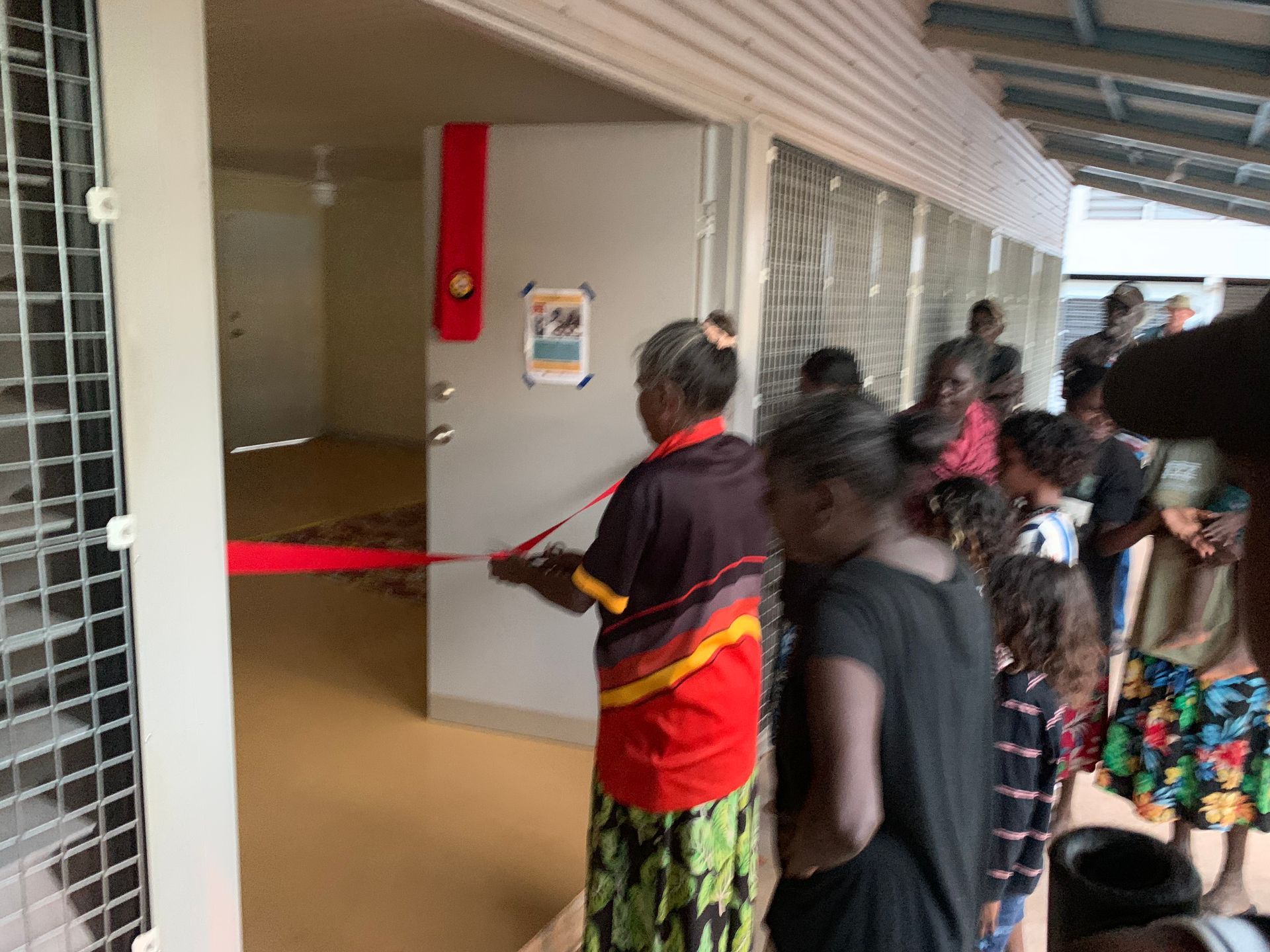 A woman is cutting a red ribbon to open a door.