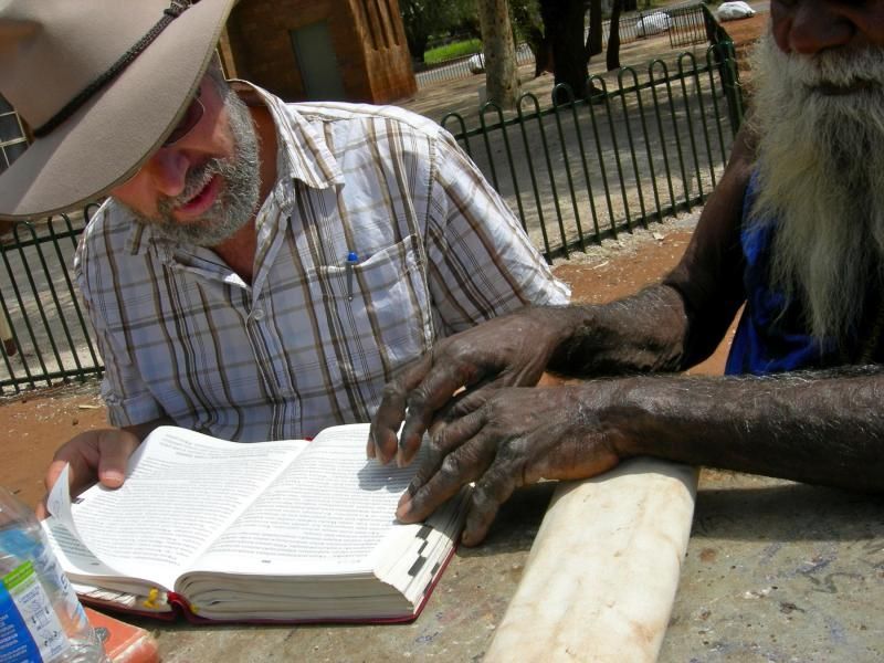 A man in a hat is reading a book to another man