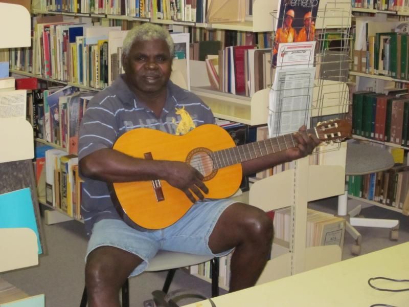 A man is playing an orange guitar in a library