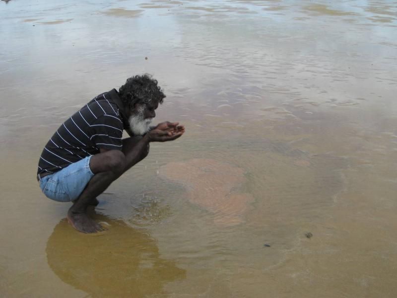 A man is kneeling in the water holding something in his hands