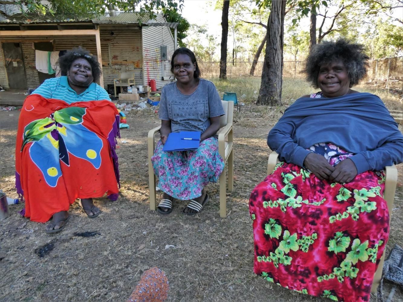 Three women are sitting in chairs outside and one of them is wearing a butterfly blanket.