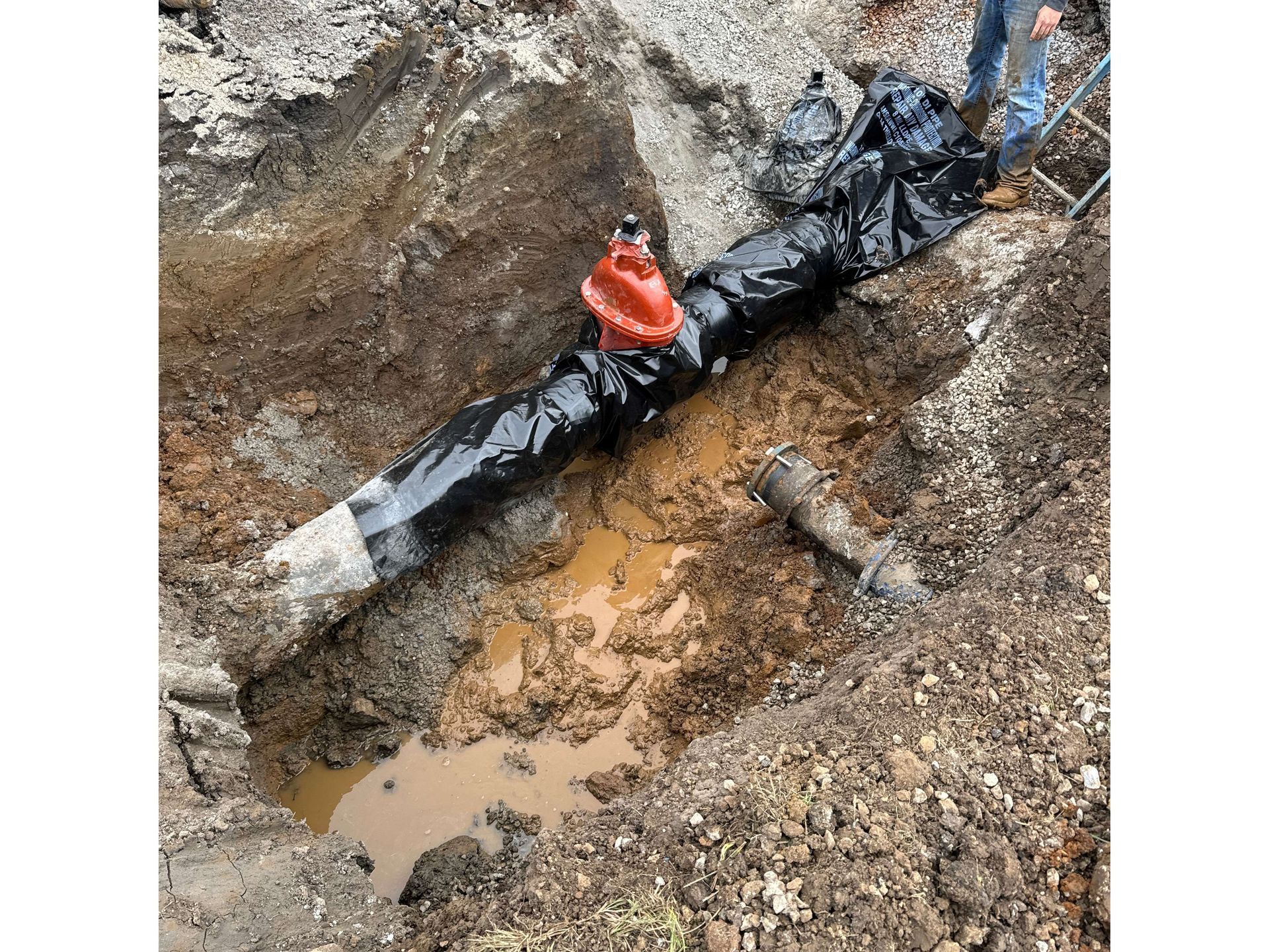 A man is standing next to a muddy pipe in the dirt.