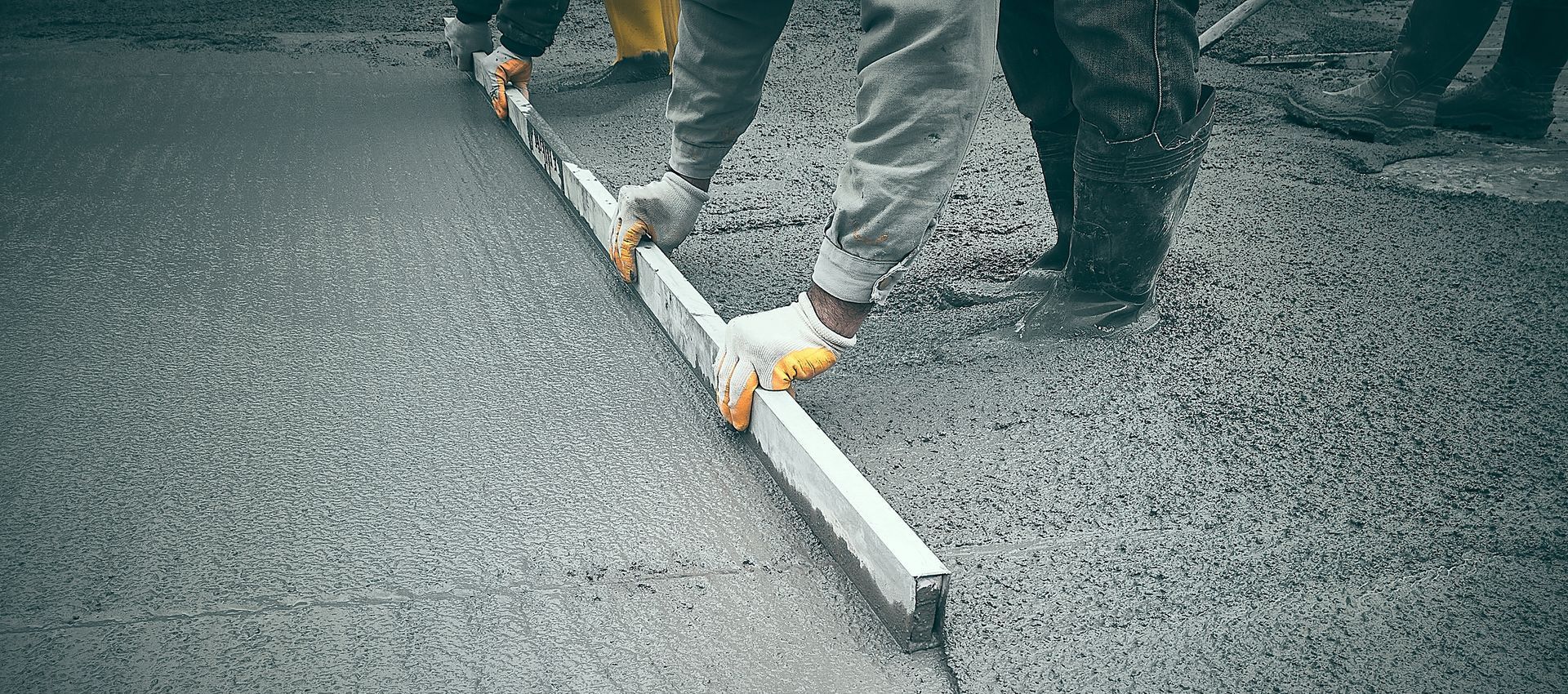 A group of people are spreading concrete on the ground with a trowel.