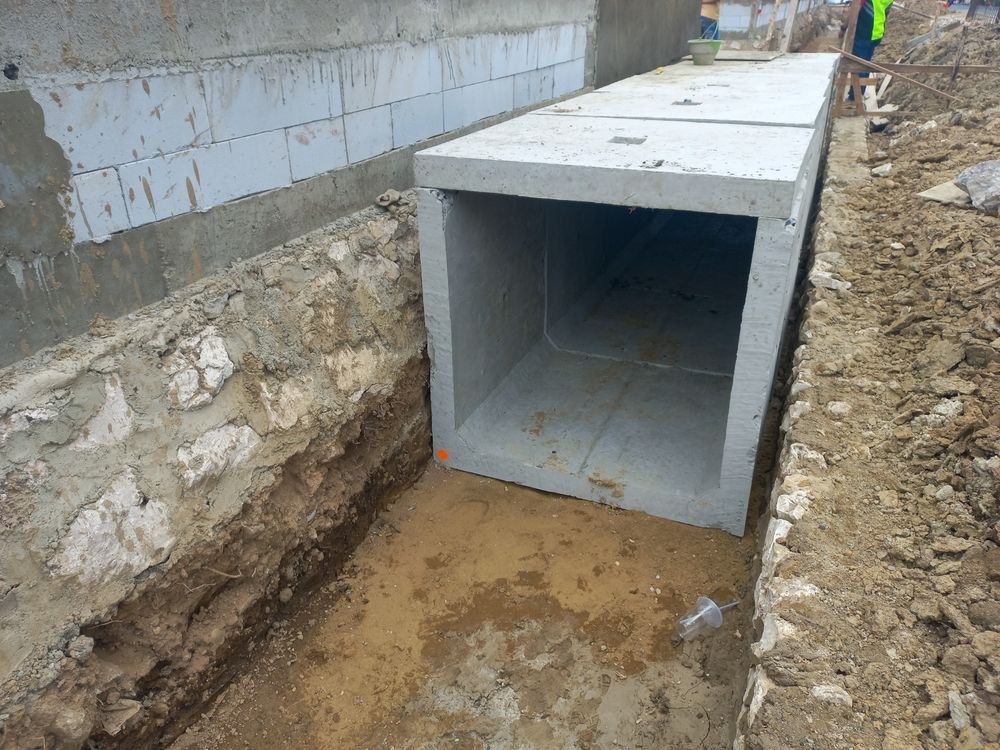 A concrete tunnel is being built in the dirt next to a wall.