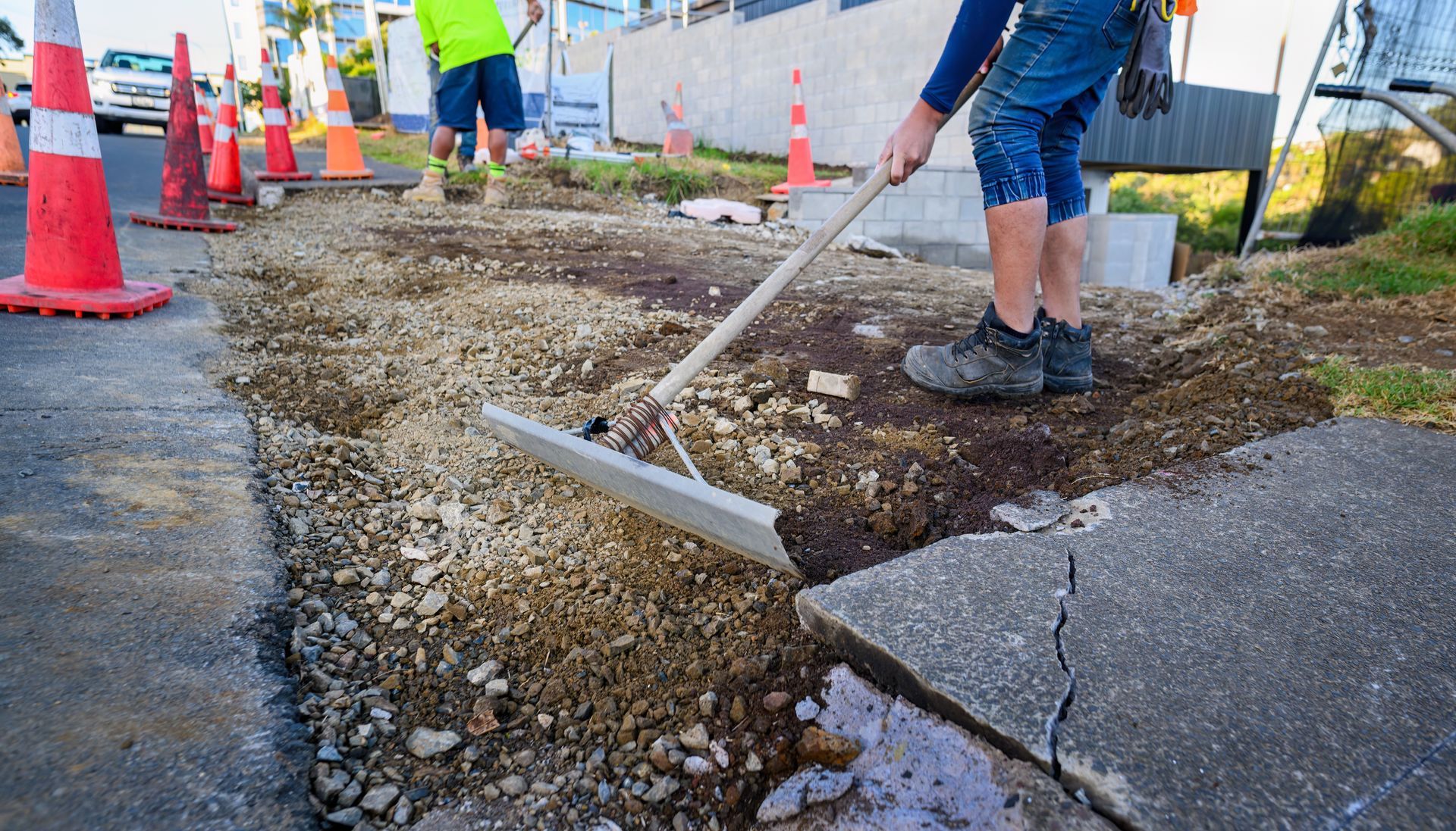 A man is using a rake to remove dirt from a sidewalk.